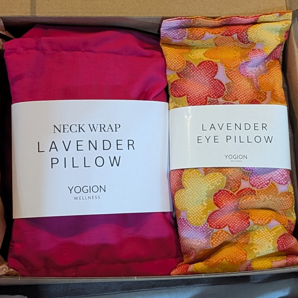 Two Yogion wellness products, a lavender neck wrap pillow and a floral lavender eye pillow, in a box.