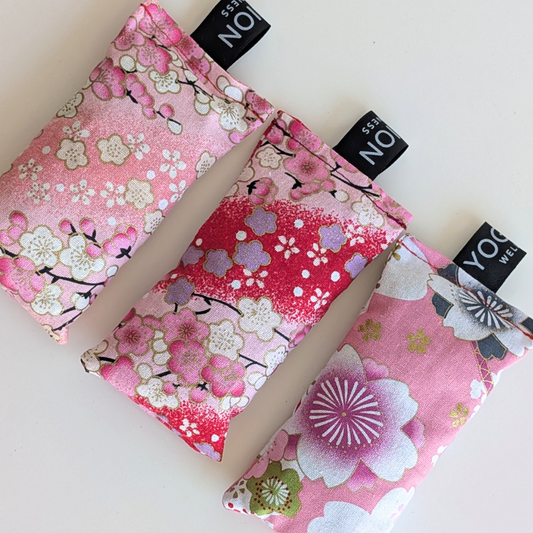 Three pink floral fabriclavender sachet bags with cherry blossom patterns on a white background by yogion wellness
