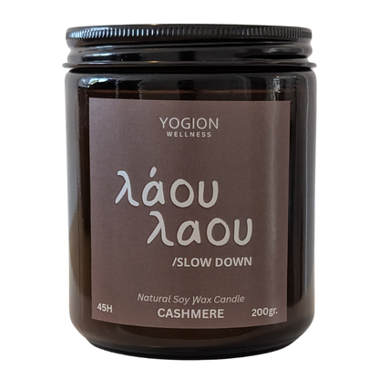 A Yogion Wellness 'laou laou' cashmere natural soy wax candle in a dark amber glass jar with a brown label and black lid, shown on a white background.