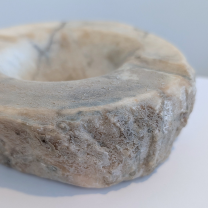 A close-up of a rustic stone ring bowl with a rough, textured surface and a shallow circular opening, for holding smudge sticks