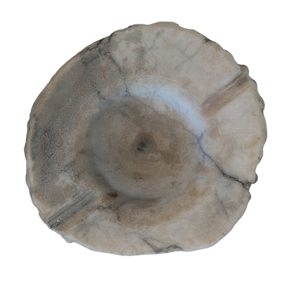 A round, handcrafted stone bowl with a scalloped edge and a textured, natural surface in shades of beige, gray, and brown, isolated on a white background.