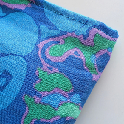 A close-up of a folded piece of fabric with a retro abstract pattern in blue, green, and pink, showing the woven texture and neat hem on a white background.